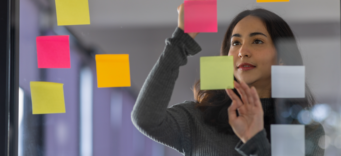 Female employee attaching sticky labels to a transparent noticeboard 